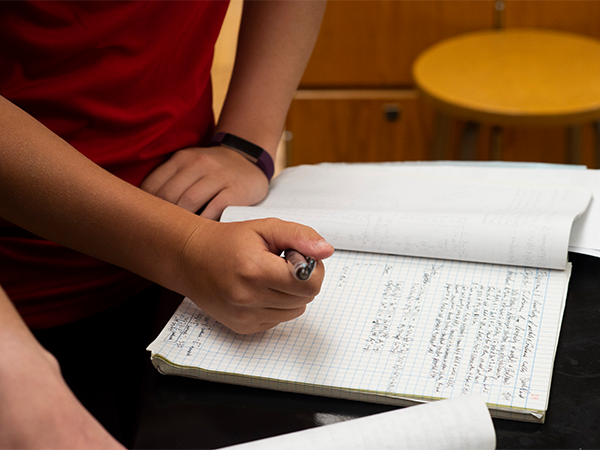 Hands of a student are visible marking down data in a notebook.